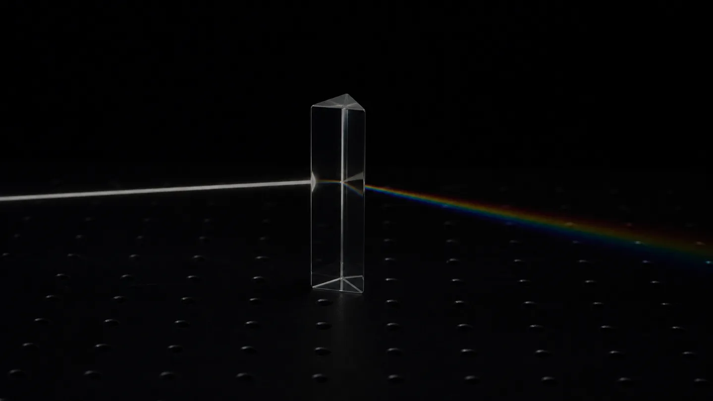 Illustrative glass prism on a dark optical surface splitting one collimated beam into a spectrum